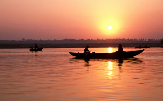 A stunning sunrise looking over the holiest of rivers in India. The Ganges. Silohuettes of boats dapple the horizon.