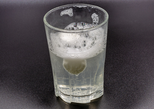 Dissolving instant effervescent tablets in a glass of water closeup on black