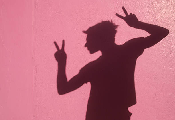 Shadow man gives two peace signs on a bright pink wall
