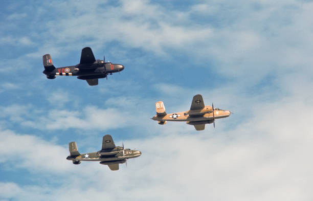 A formation of three B-25 Mitchell medium bombers flies by overhead.  All aircraft appear as they would have have during World War II.  The left most aircraft is painted in the colors of the British Royal Air Force.