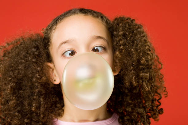 Little girl blows a big bubble from gum on a red background.