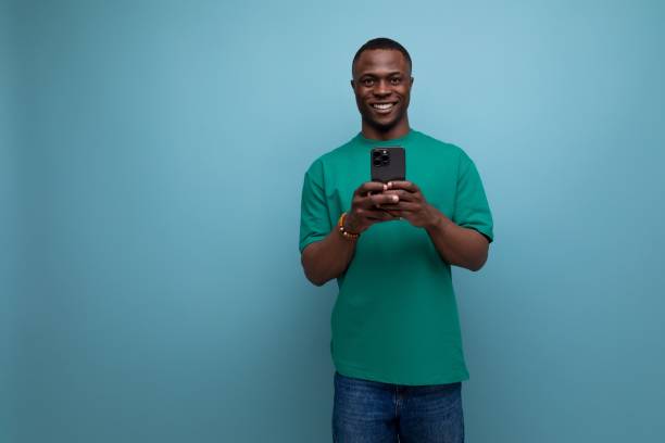 istock young handsome african guy with a short haircut dressed in a basic t-shirt uses a smartphone to communicate on a blue background with copy space 1726955374