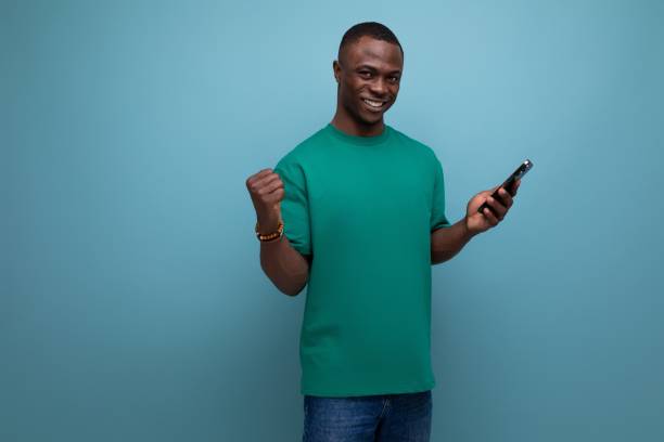istock young handsome african guy with a short haircut dressed in a basic t-shirt uses a smartphone to communicate on a blue background with copy space 1726955572