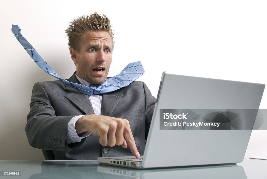 Stressed Young Businessman Using Laptop Computer at Desk Terrified businessman tries to hit the panic button on his computer before it's too late Humor Stock Photo