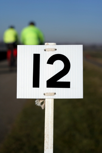 Number twelve marker post, indicating miles gone for races (running, biking) - two bikers in soft focus in the background, england