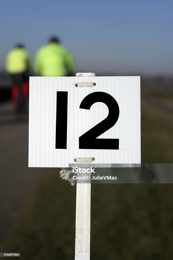 Number Twelve Number twelve marker post, indicating miles gone for races (running, biking) - two bikers in soft focus in the background, england Competition Stock Photo