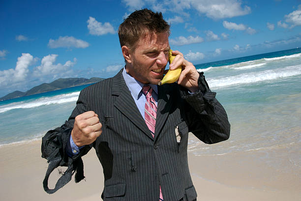 castaway frustrato uomo d'affari parla sul telefono cellulare banana - stranded beached beach businessman foto e immagini stock