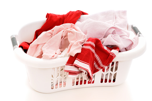 Assorted female clothing items in white plastic laundry basket on white background