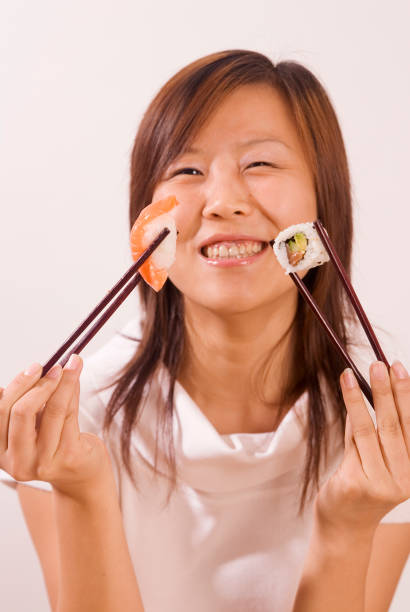 Young Asian Girl With Chopsticks Ans Sushi Food Young Asian woman with sushi between the stalls - nigiri and maki kids eating tuna stock pictures, royalty-free photos & images