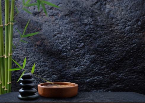 Balanced Stones and Wooden Water Bowl with Bamboo and Leaves against a Dark Background.