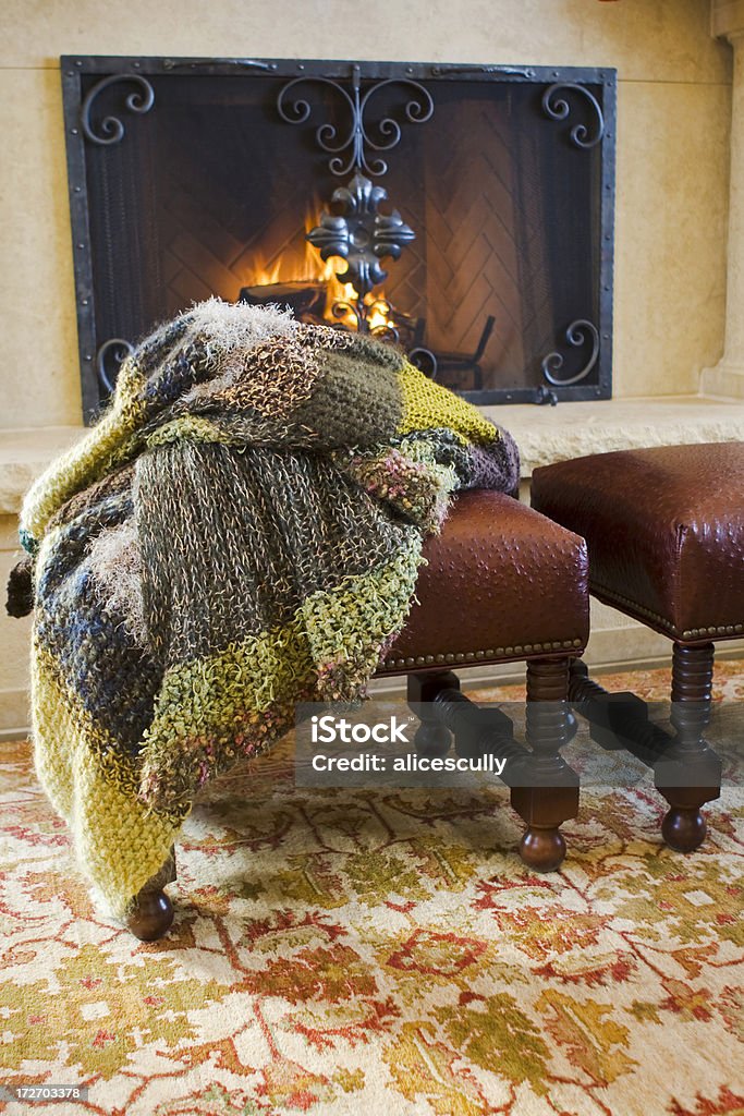 Handknit Wool Afghan Cozy scene of a multi-colored handknit wool afghan on leather stools in front of fire in fireplace. Blanket Stock Photo