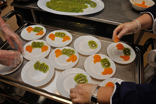 A caterer prepares plates of dessert with slices of kiwi fruit and orange.