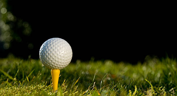 Golf Ball on Tee - Panoramic Golf Ball on grass and a dark background. Very shallow Dof - Focus is on the ball and tee night golf stock pictures, royalty-free photos & images