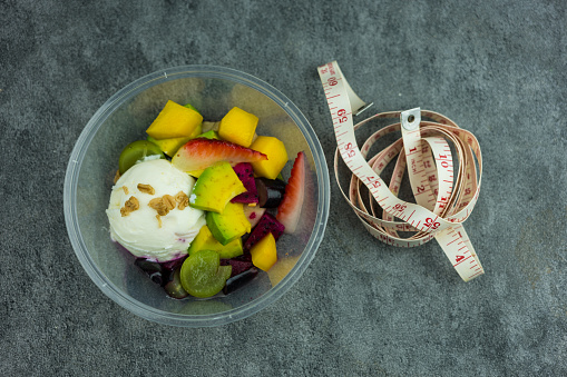 Fruit salad and fresh yogurt with white measuring tape. Healthy food for fitness. Lunch box. Top view.