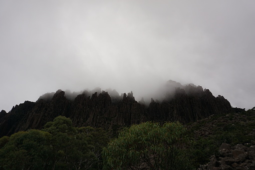 Dramatic moody view of rocky spiky ridge disappearing in low hanging clouds, cloudy weather in cradle mountain, tasmania, australia