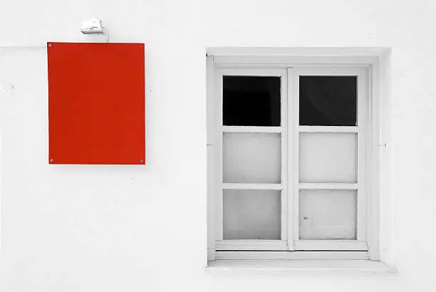 Facade with a bright red and blank notice board. Mostly desaturated, except for the bulletin board.