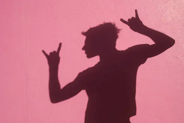 Shadow man gives 'rock on' hand sign against a vibrant pink wall