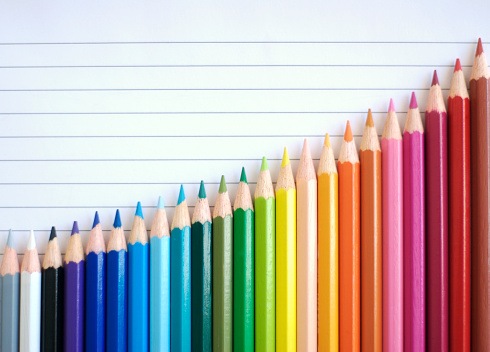Bar chart graph rainbow of colored pencils slide up against a sheet of lined paper sloping in a good direction of success