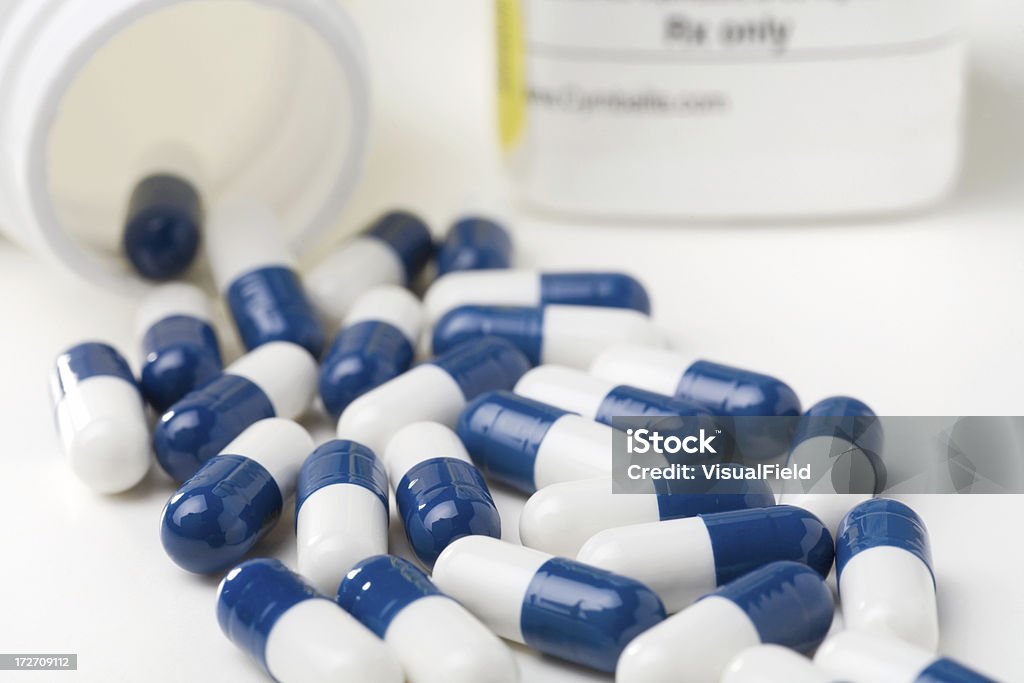 Medicine Capsules Spilled from Prescription Bottle blue & white capsules spilling from prescription bottle Blue Stock Photo