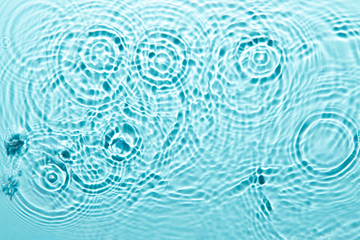 Defocus blurred blue color water ripple surface clear calm texture background with splashing bubbles water drop. Abstract and nature concept. Shiny water wave sunlight reflection shining copy space.