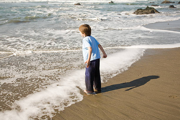 Boy on Edge of water Child playing at the ocean edge. mm1 stock pictures, royalty-free photos & images