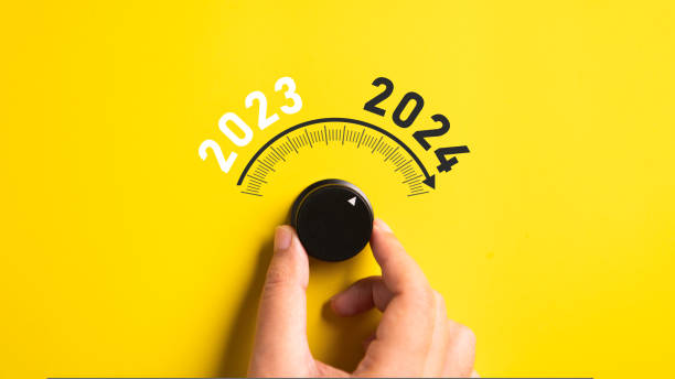 Close up of a hand adjusting volume button from year 2023 to 2024 on isolated yellow background. Happy New Year celebration concept. stock photo