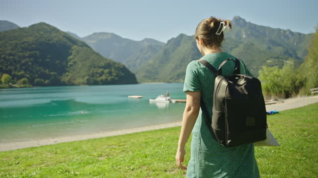 SLO MO Young Woman with Backpack Walking towards Lake Garda along Mountains on Sunny Day during Vacation