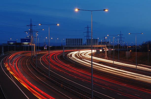 Power On The Move Electricity pylons in the background as traffic thunders around the Manchester, UK, M60 orbital motorway. Power generated and power used. night freeway stock pictures, royalty-free photos & images