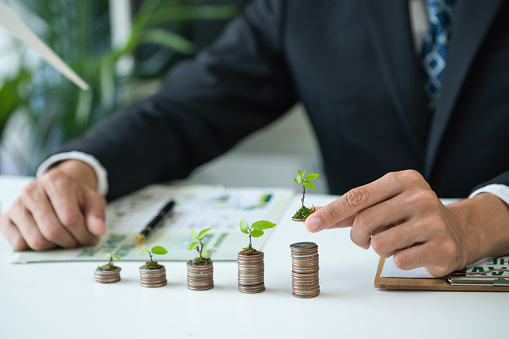 Businessman with coin stack at his office as sustainable money growth investment or eco-subsidize. Green corporate promot and invest in environmental awareness. Gyre