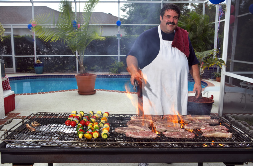 Shell steaks and kabobs on large barbecue being prepared by chef.