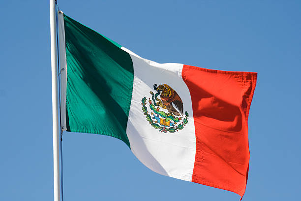 Mexican Flag, National Banner of Mexico Waving Against Blue Sky Horizontal view of a Mexican national flag waving in the wind against a clear blue sky. mexican flag stock pictures, royalty-free photos & images