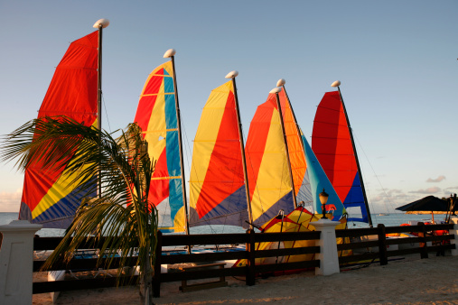 Six beached catamarans in front of a wooden fence overlooking the ocean taken at sunset with clear blue sky.