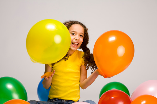 Little girl playing in balloons holds up 2 balloons