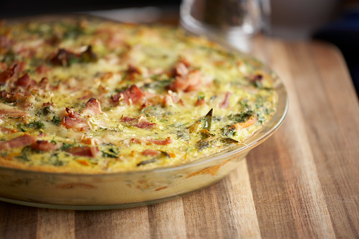 Home made egg and bacon and potato frittata on wooden board. Very shallow DOF near front of dish.