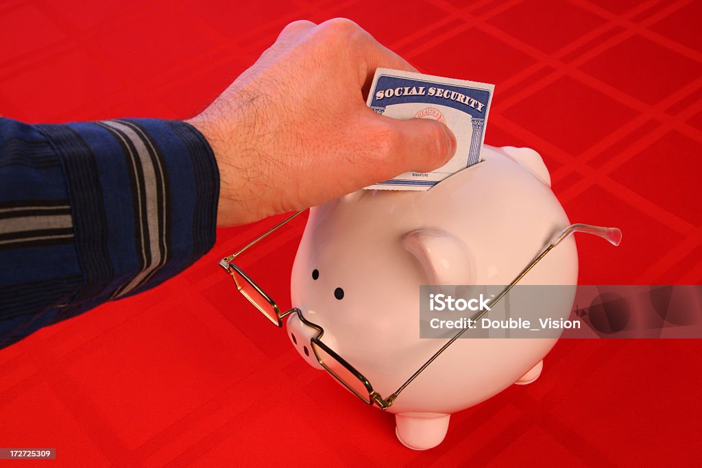 Hand Depositing Social-Security Card into Piggy Bank with Glasses This photo has a hand depositing a Social Security card into a piggy bank wearing elderly spectacles over a red background. Social Security Card Stock Photo