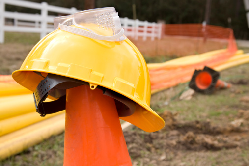 Construction of a new gas pipeline along side of a rural road.  Hardhat and safety goggles left on top of an orange safety pylon cone.