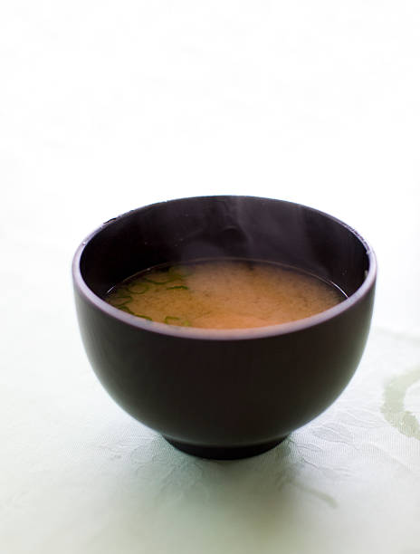 A bowl on miso soup on fancy white tablecloth.  The DOF is narrow enough that the tablecloth at the top of the image blurs out to white for copyspace.  Focus point is on the back of the bowl where the soup meets th bowl.