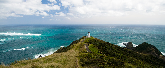 Distant tourists walk to the lighthouse at the northern tip of New Zealand's North Island, where the Pacific Ocean and Tasman Sea meet.