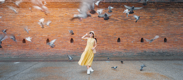 Young asian woman traveler in Yellow dress with hat and bag traveling on Tha Pae Gate, Tourist visit at the old city in Chang Mai, Thailand. Asia Travel, Vacation and summer holiday concept