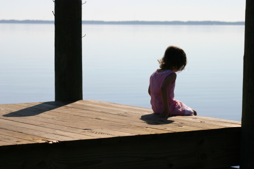Little girl sitting quietly on the wooden dock by the bay. Copy space!