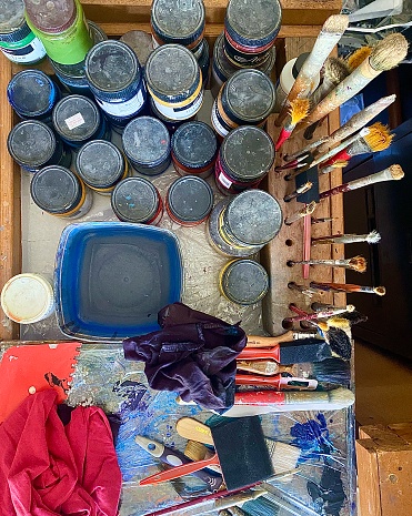 Vertical flat lay of painting artists table filled with acrylic paints, brushes, sponges, materials and paint equipment seen in creative studio