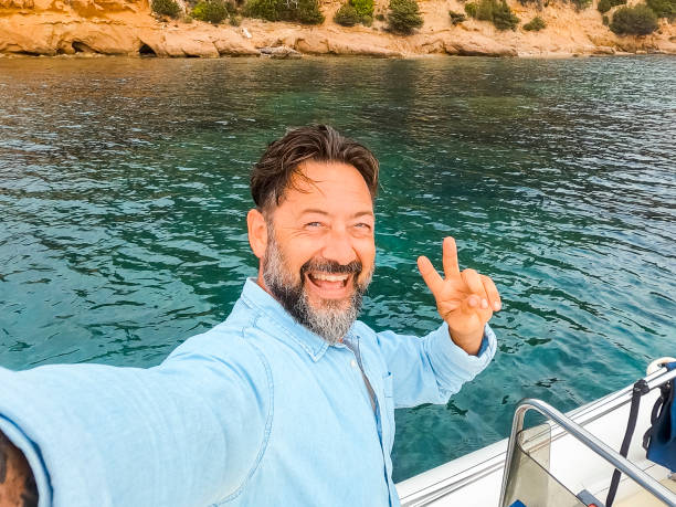 One cheerful happy man with excited expression on face taking selfie picture standing inside a boat during sea excursion tour in summer holiday travel vacation. Male people enjoying life and tourism