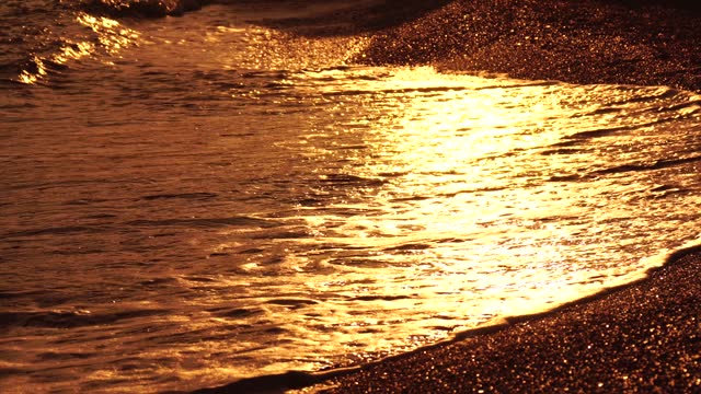 Golden sunset on the beach. Foamy waves rolling towards golden sand beach under low warm sun light. Slow motion. Nobody. Holiday recreation concept. Abstract nautical summer ocean sunset nature.