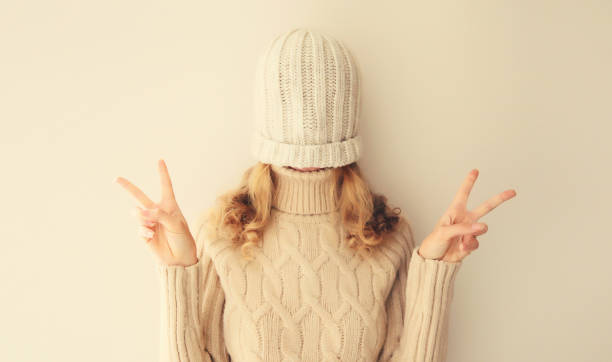 istock Cheerful funny woman having fun, pulling winter hat over her face and covering her eyes wearing warm soft knitted clothes, sweater on beige studio background 1727348326