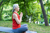Senior latin woman doing yoga training exercise wearing red sportswear. Old lady with grey hair making fitness relaxation exercise.