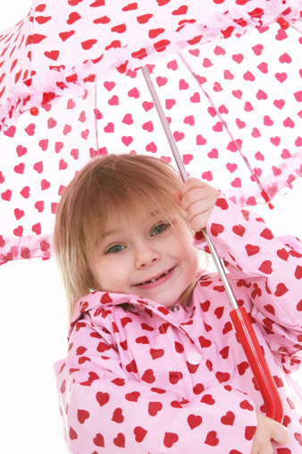 Little girl in a pink rain jacket with hearts holding an umbrella