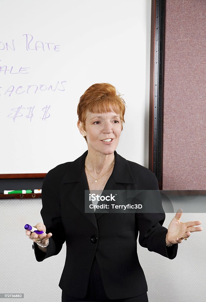 Woman Instructor Explaining Business Finance Concept to Class Corporate trainer at a whiteboard.Complete series: Hand Sign Stock Photo