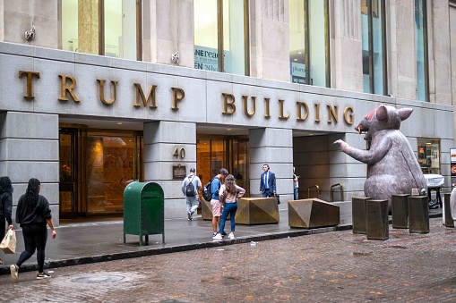 New York, NY, USA  10-06-2023 Pedestrians on sidewalk and cobblestone street in front of Trump Building in the financial district of New York City. A giant inflatable rat is in front of the door facing the entrance. View from behind. Copy Space. Editorial use only
