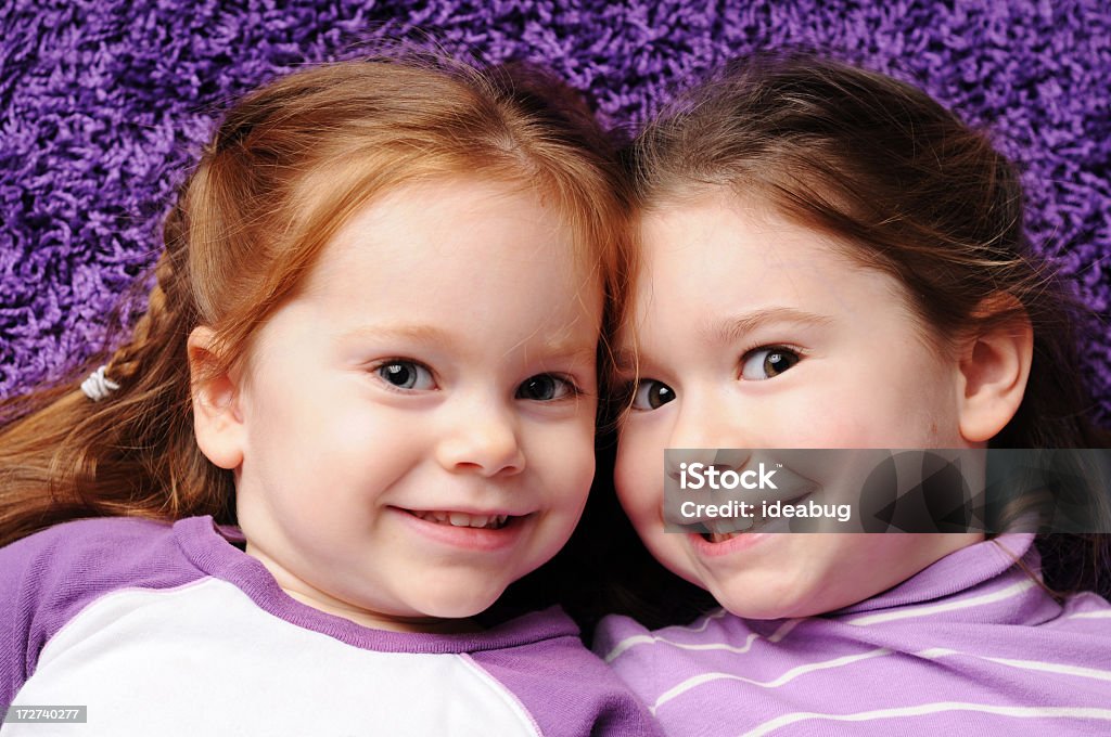 Duas irmãs feliz deitado no tapete roxo - Foto de stock de 2-3 Anos royalty-free