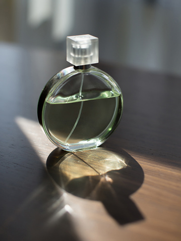 Perfume bottle on a wooden table with sun light and shadow